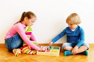 Two cute kids, little brother and his big sister playing board games at home, wearing funny socks